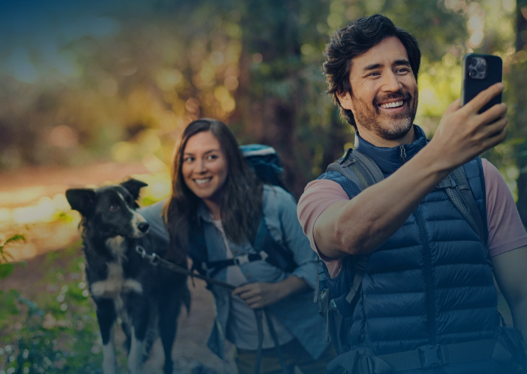 Couple taking a selfie in the woods with their dog during sunset