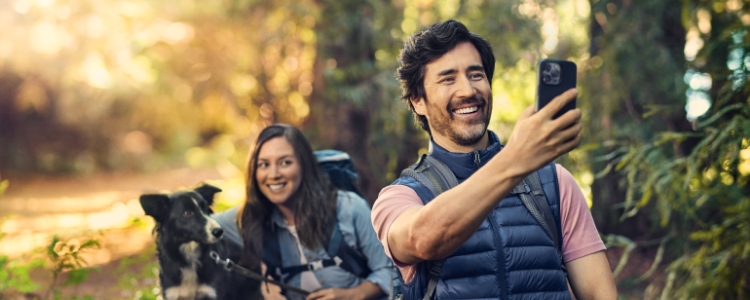 Couple taking a selfie in the woods with their dog during sunset